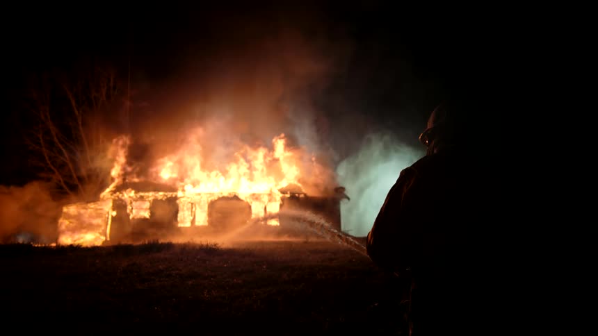 Firefighter battles a burning house at night with a water hose