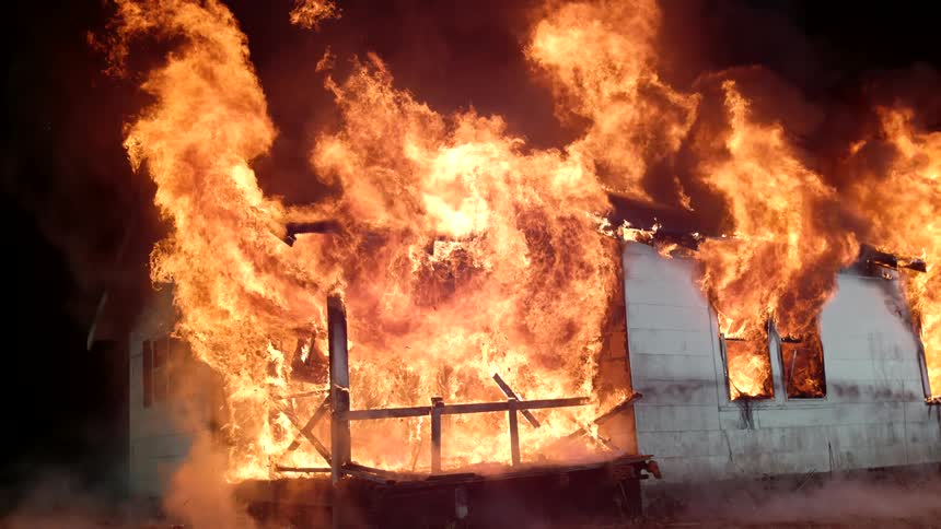 Raging flames engulf a burning a building as water from a firehose flies through the air