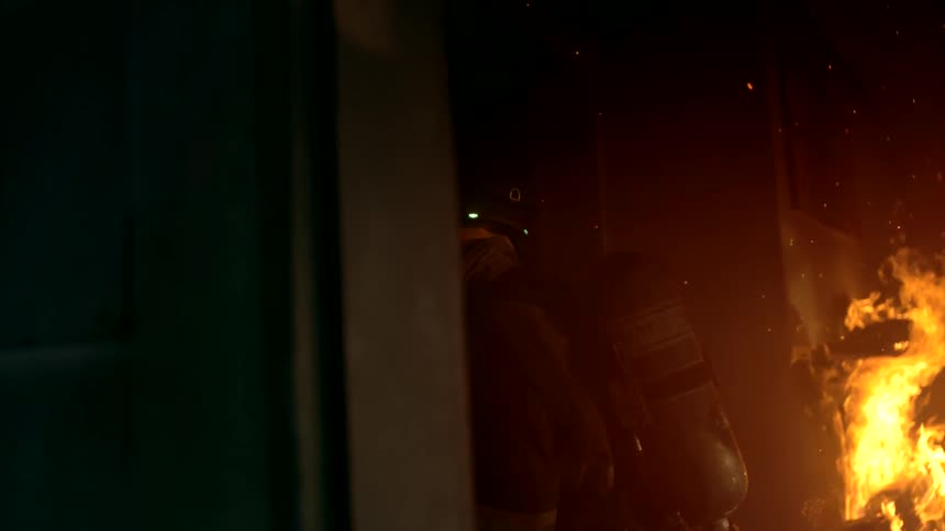 Firefighter walks past a burning fixture in a smoky building