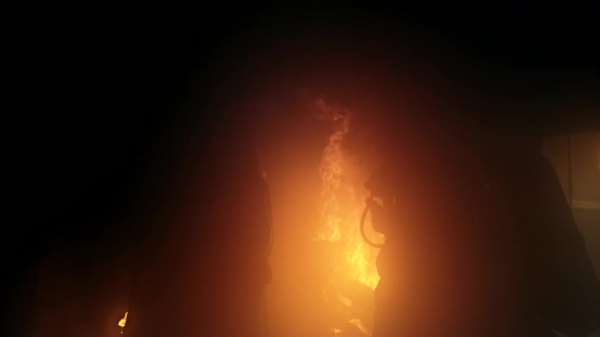 Two firefighters battle a blaze silhouetted in thick smoke