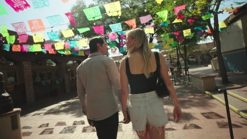 A couple walking hand in hand on a sidewalk where there are several flags hanging on the street