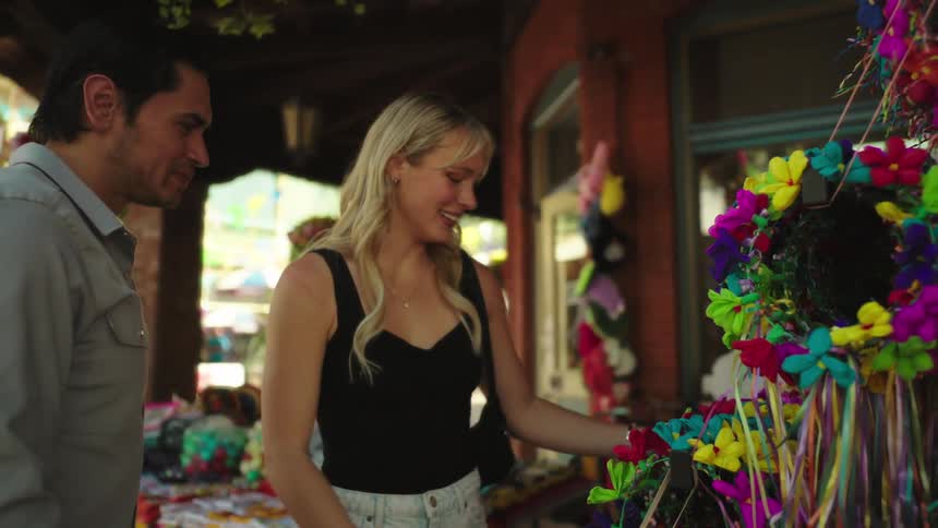 A man and a woman are looking at a colorful wreath decorated with artificial flowers and ribbons outside a shop