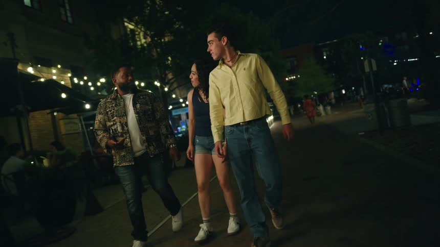 Two men and a woman walking in a square at night