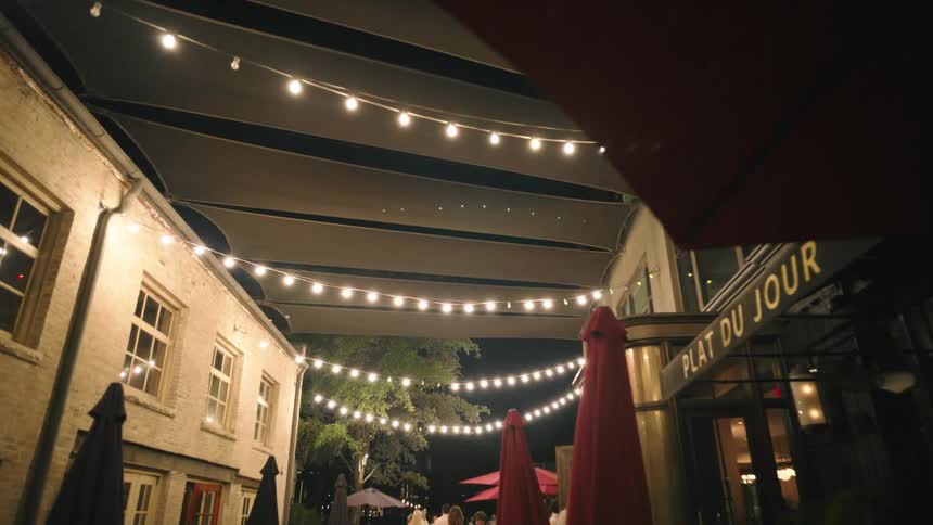 Pedestrians walk past the outside seating of a cafe at night under a translucent street cover