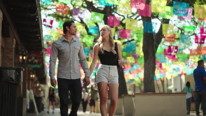 A man and a woman holding hands walking through a public place
