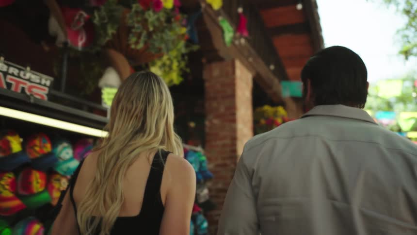 A man and woman walk through a colorful outdoor market browsing vibrant merchandise