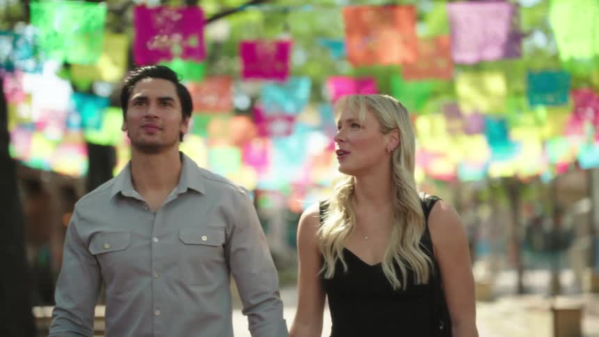 A man and a woman holding hands walking down a street decorated with small flags