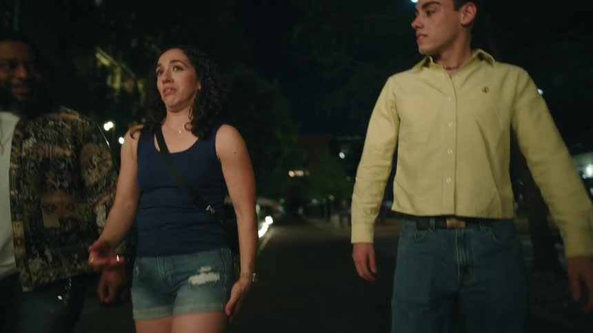 Two men and a woman walking and talking on a city street at night