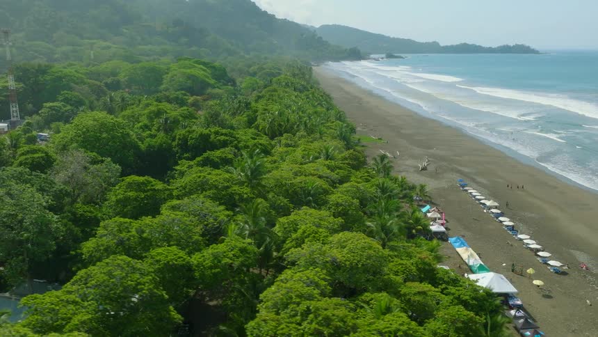 Aerial view of a tropical beach with umbrellas vendor stalls and dense forest