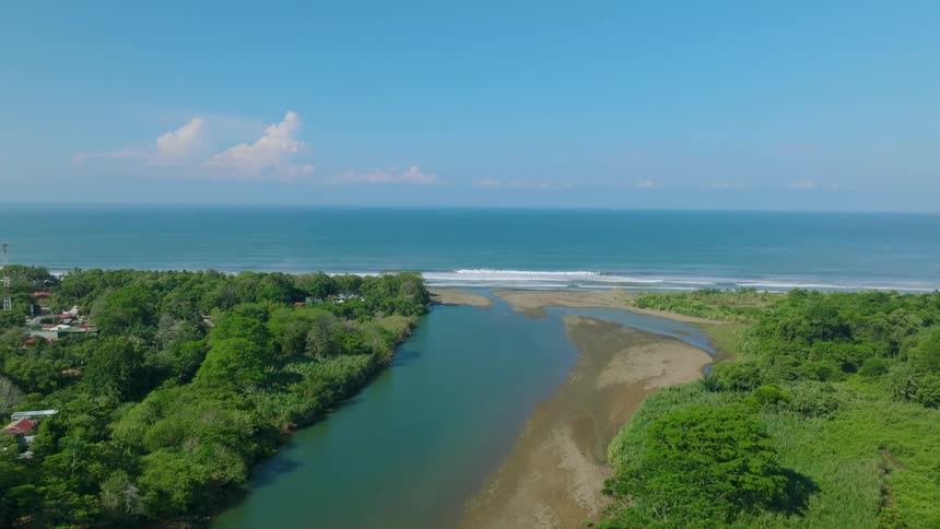 An aerial view of a river with forests on the sides and a connection to the sea in the background