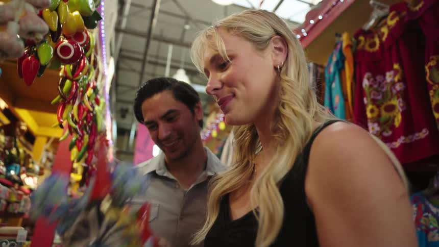 A woman and a man in a handmade goods store the woman picks up a handcrafted ornament with a flower inside and smells the flower