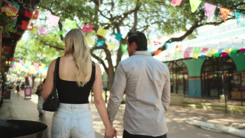 A couple holding hands walking through a fair and stopping to look at handmade products