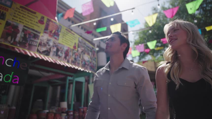 A man and woman walk along a street decorated with colorful banners and street vendors
