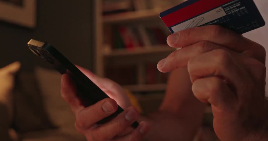A mans hands are shown in fast motion holding a credit card and tapping the screen of a smartphone repeatedly