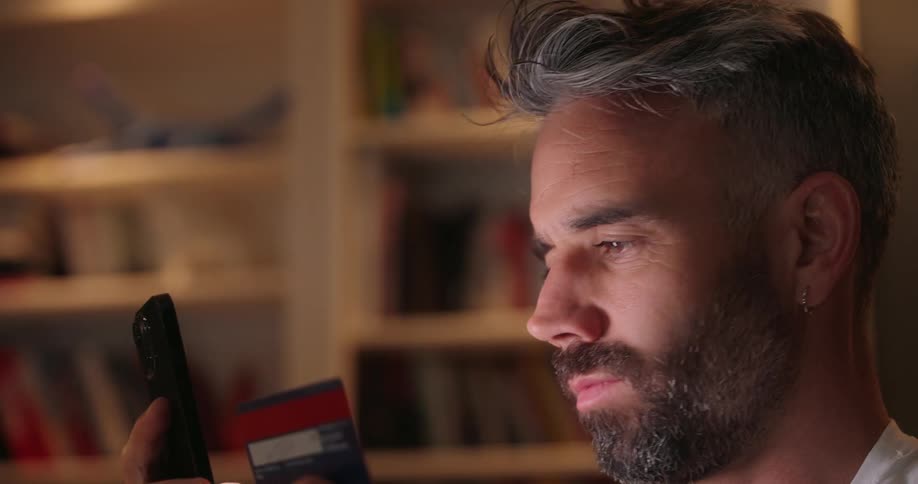 A man enters credit card information into his smartphone indoors