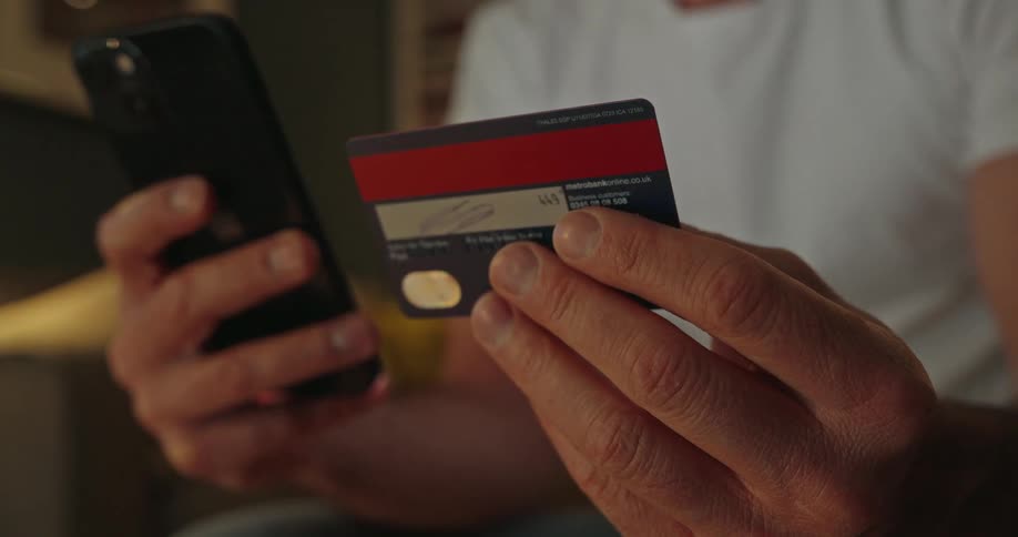 A man holding his credit card is typing the numbers into his phone