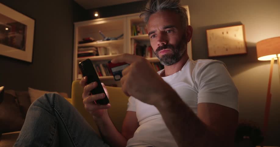 A man sits in his living room and enters credit card info into his smartphone