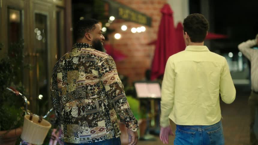 Two men talking and walking down a street lined with restaurants