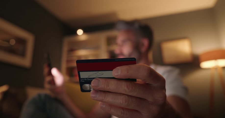 A man holds his credit card in one hand and types of his phone with the other