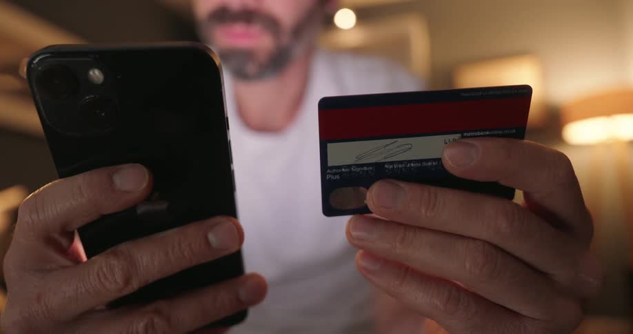 Man seated in a room types credit card details on his mobile phone