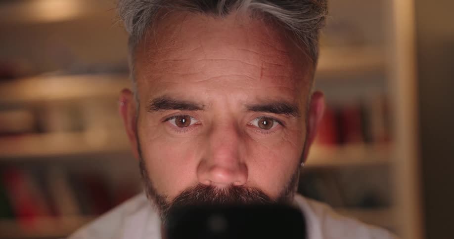 Face of a man in a room starring straight at his mobile phone