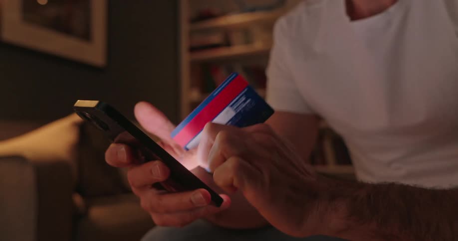 Hands of a man typing on his mobile phone while holding a credit card