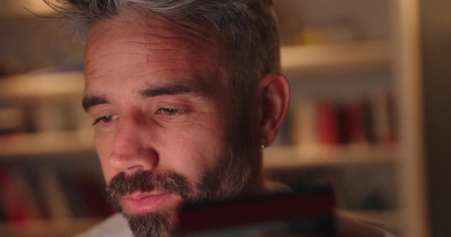 The face of a bearded man who is frowning while looking at a credit card in front of him