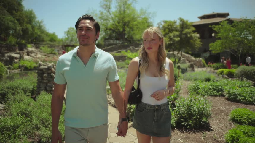 Couple holding hands strolling on a stone path through a botanical garden