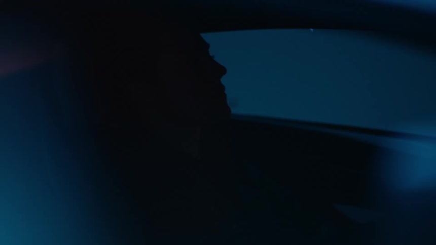Man silhouetted while sitting in a vehicle is sometimes lit by red lights