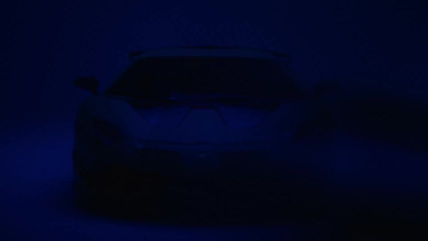A white lamborghini aventador svj with black racing stripes is bathed in dim blue light against a matching backdrop