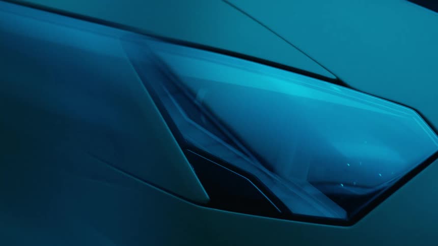 A closeup of the lamborghini aventador svjs headlight illuminated by intense blue lighting that highlights its sharp design