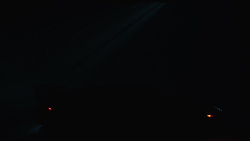 A shadowy scene with a barely visible car dimly lit by taillights and faint overhead light