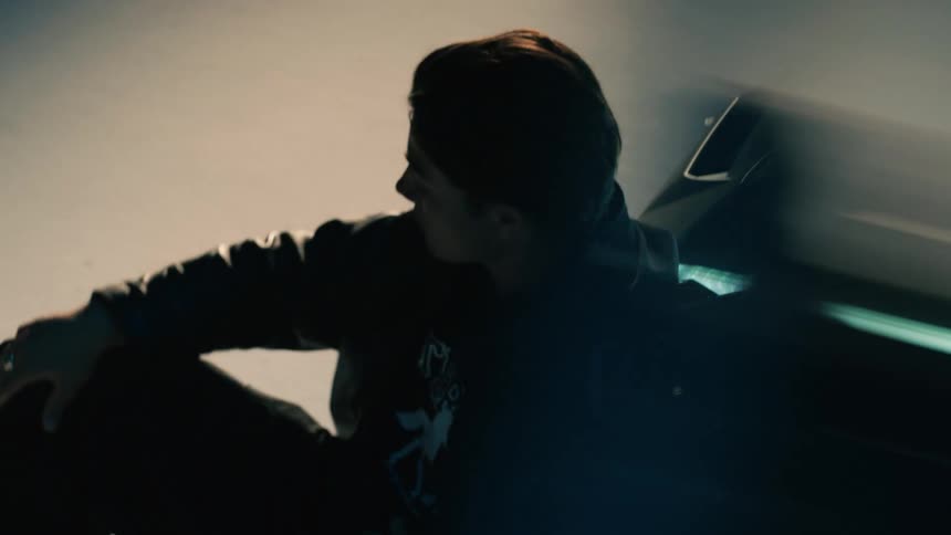 A man sitting on the floor next to a car inside a garage