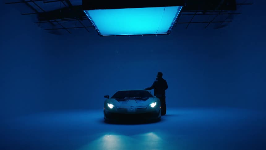 Silhouette of a man next to a lamborghini in a studio with blue lighting