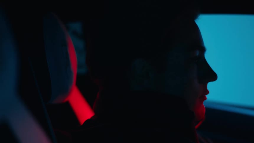 A man is in a car as lights flash in the darkness outside