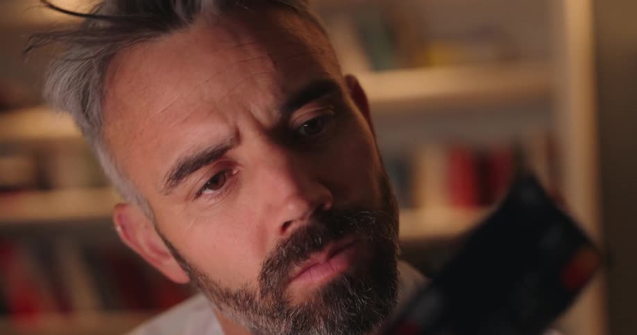 Seriouslooking man looks closely at a card in a softly lit indoor setting