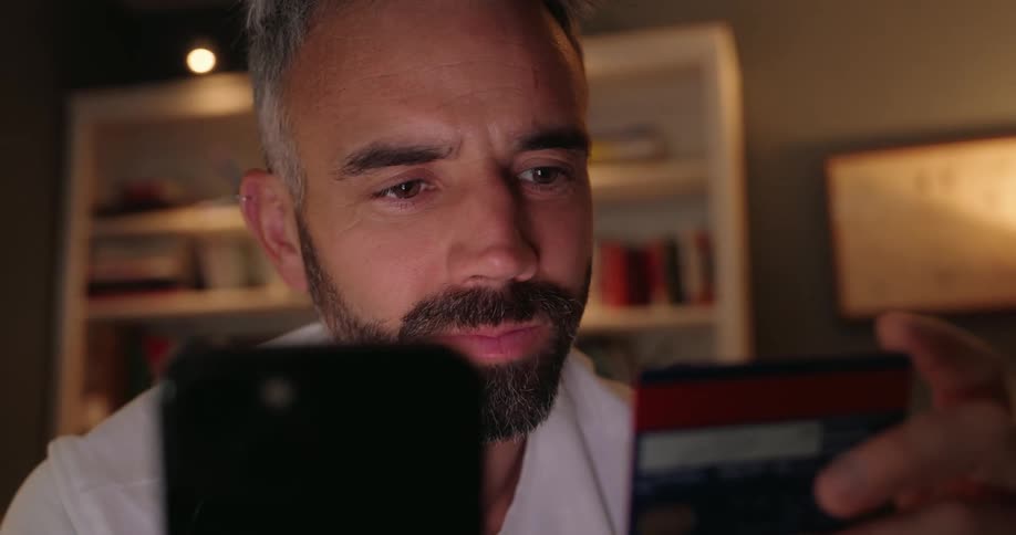 A man holds a credit card in one hand and a smartphone in the other and looks back and forth
