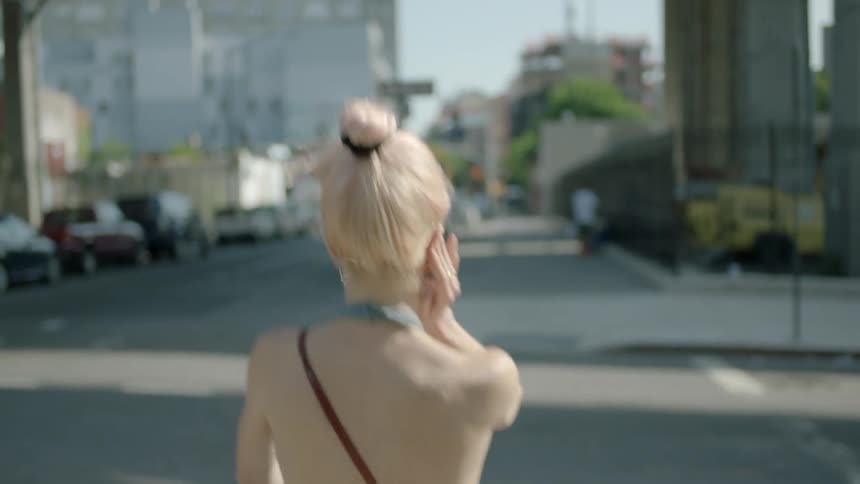 A blonde woman walks across a city crosswalk