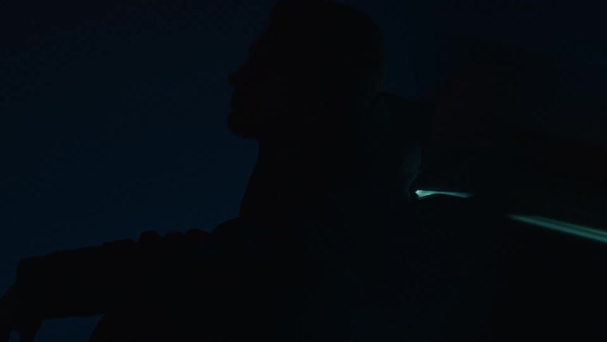 A man is sitting leaning against a sports car in the dark