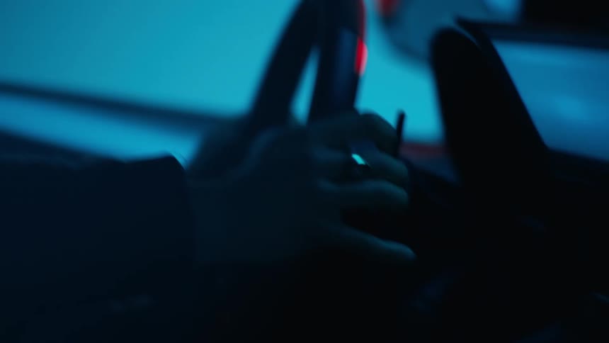 Closeup of a person driving a sports car hands gripping the steering wheel under blue and red lights
