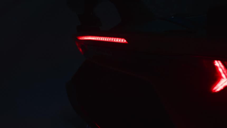 The illuminated red taillights of a dark sports car are shown in a closeup