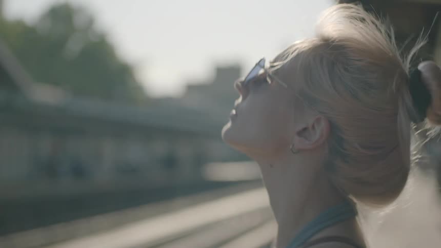 A woman waits for a train at a station on a sunny day