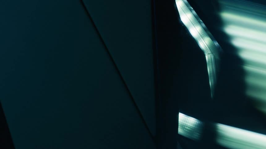 A close up of the front headlight of a modern sports car under flashing lights in a dimly lit room