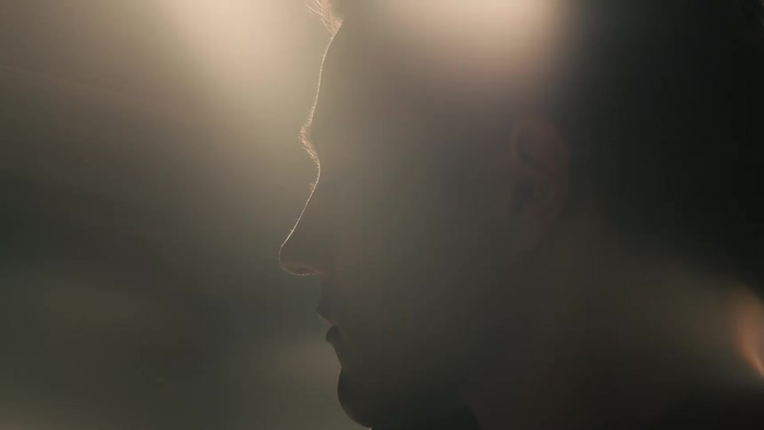Closeup profile of a young man with a modern sleek appearance under flashing lights in a dimly lit room with overhead lighting
