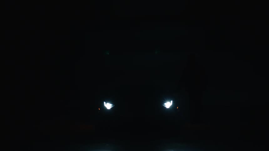 A man walks over to the sports car in the dark