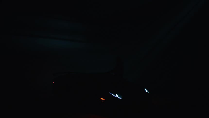 Person walking towards a sports car with headlights on is parked in a dark studio illuminated by a blue overhead light
