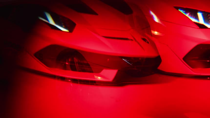 A lamborghini is parked in a dark environment with its headlights on and a red light illuminating the surroundings