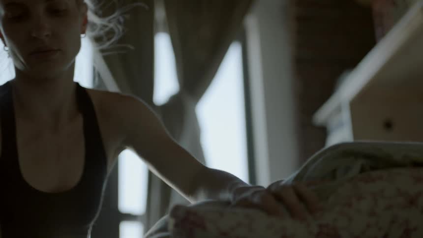 A woman adjusts a pillow and blanket on her bed