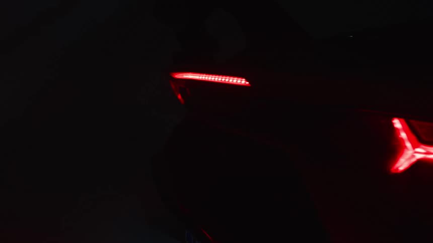 A sleek sports cars illuminated tail lights glow red in a dark moody studio setting