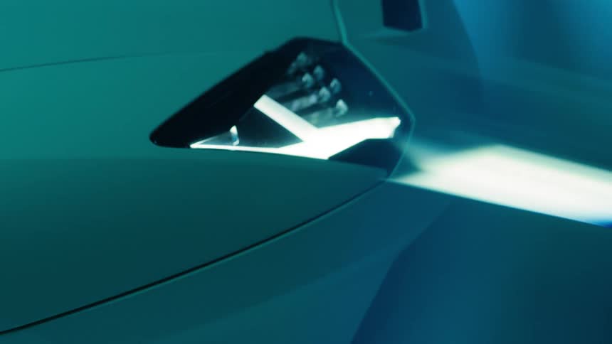 A lamborghini with its headlights turned on sits in a dark room with flickering blue light